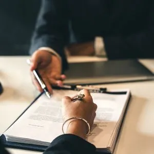 Pessoa assinando um contrato sob a orientação de um advogado, representando litígios e renegociação contratual.