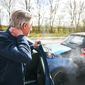Homem analisando um carro danificado após um acidente, representando casos de dano material, dano moral, lucros cessantes e danos existenciais.