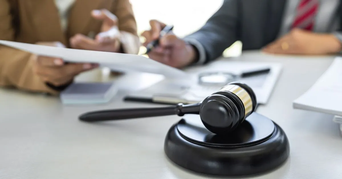 Imagem de um martelo de juiz em destaque sobre uma mesa, com advogados analisando documentos ao fundo, representando consultoria jurídica e litígios civis.