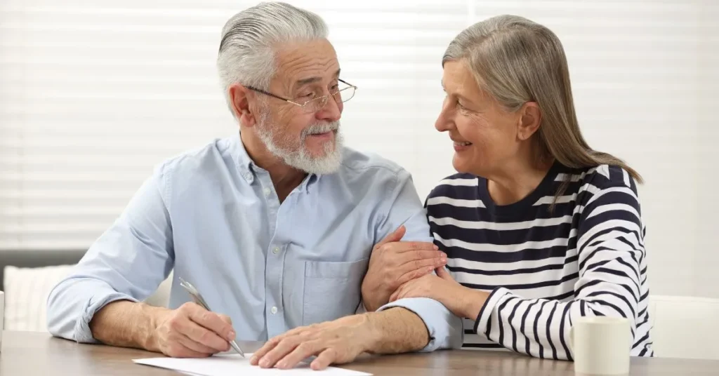 Casal idoso sorridente preenchendo um documento juntos, representando a importância do testamento na proteção da família.