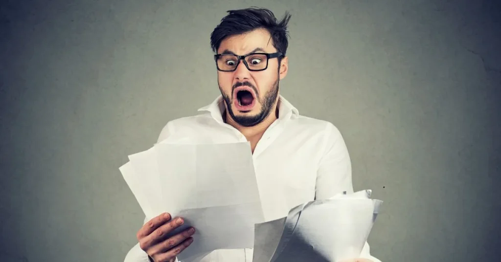 Homem assustado ao ver papéis e contas, representando a surpresa e frustração com a inadimplência no aluguel.