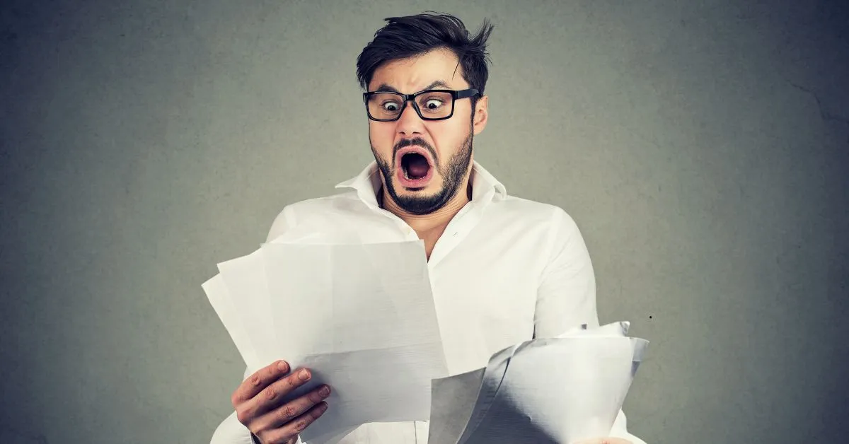 Homem assustado ao ver papéis e contas, representando a surpresa e frustração com a inadimplência no aluguel.