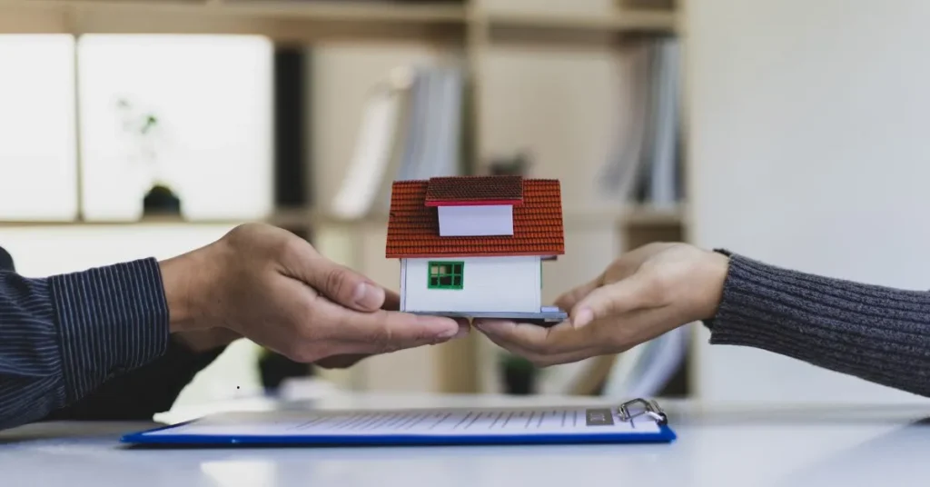 Duas mãos segurando uma miniatura de casa sobre um contrato, simbolizando a divisão de herança e as responsabilidades dos herdeiros.