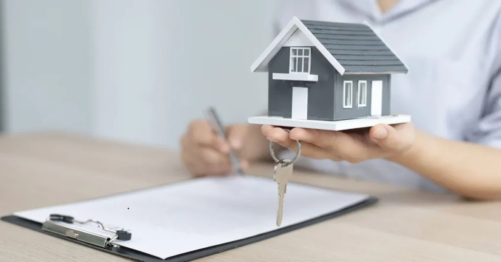 Pessoa segurando miniatura de casa com chave e assinando contrato, representando a diferença entre posse e propriedade de um imóvel.