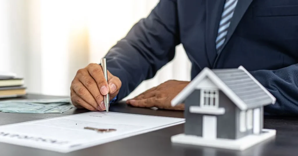 Homem assinando documento de regularização de imóvel com miniatura de casa sobre a mesa, representando o processo de usucapião.