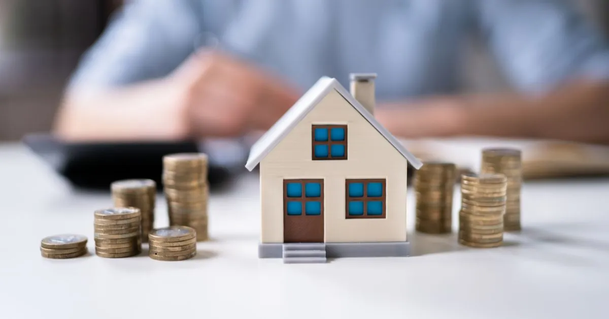 Miniatura de casa entre pilhas de moedas simbolizando revisão de aluguel e equilíbrio de valores