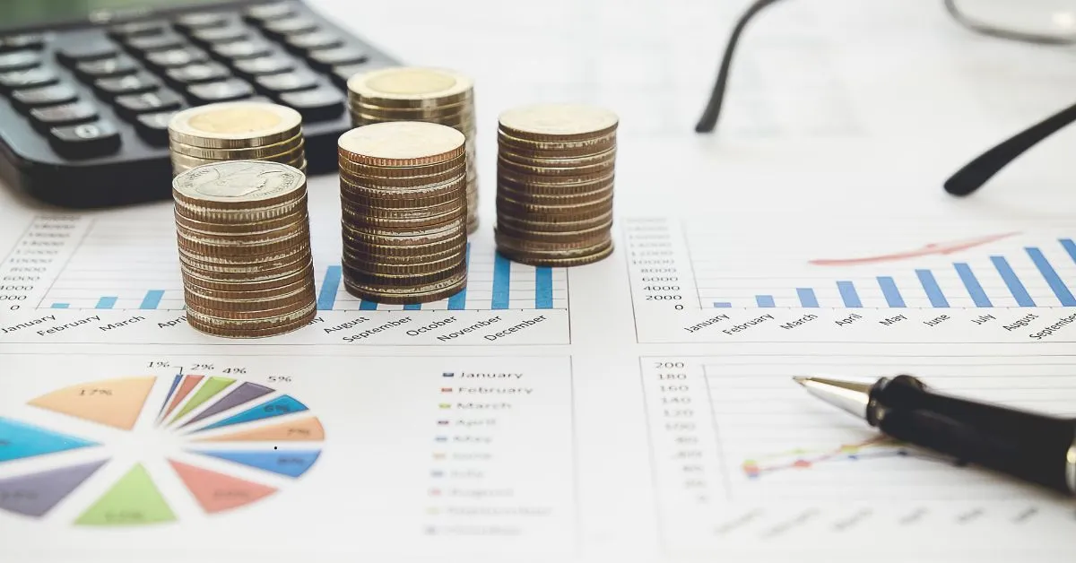 Pilhas de moedas sobre gráficos financeiros, representando recolhimentos em atraso do contribuinte individual
