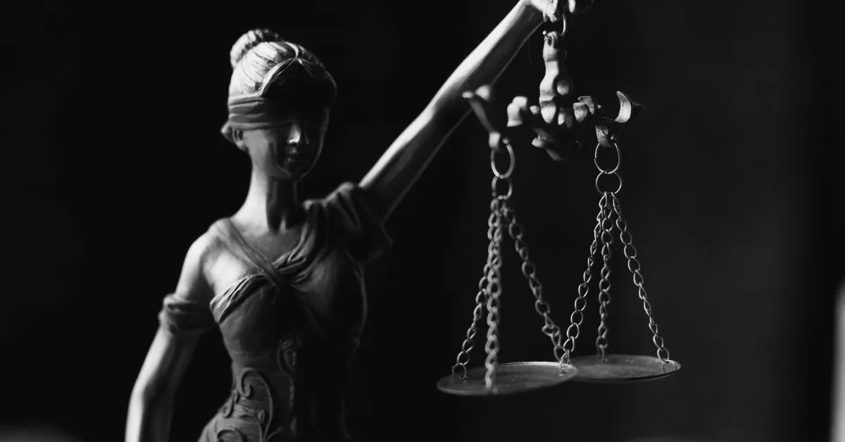 Estátua da justiça segurando balança em fundo escuro, simbolizando o julgamento de ações por dano moral.