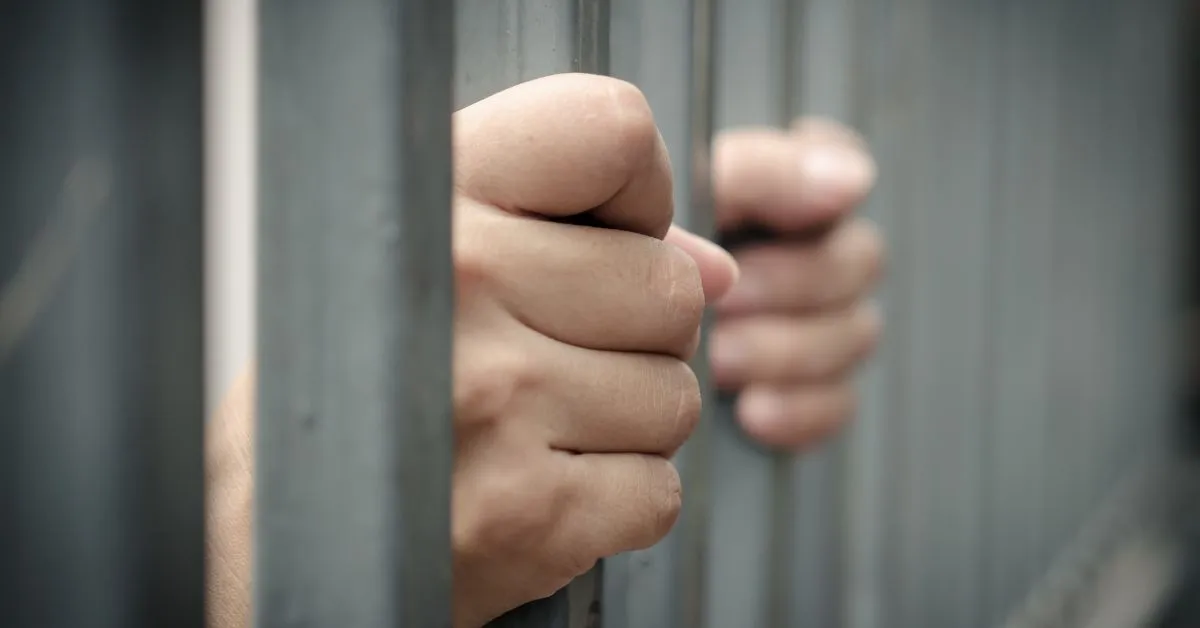 Réu primário tem direito a liberdade ilustrado por mãos segurando grades de prisão