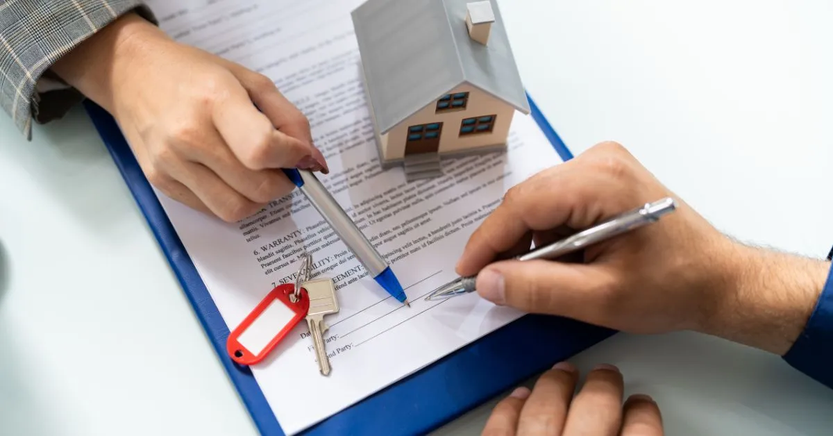 Pessoa assinando contrato de compra de imóvel usado com chave e miniatura de casa sobre o documento