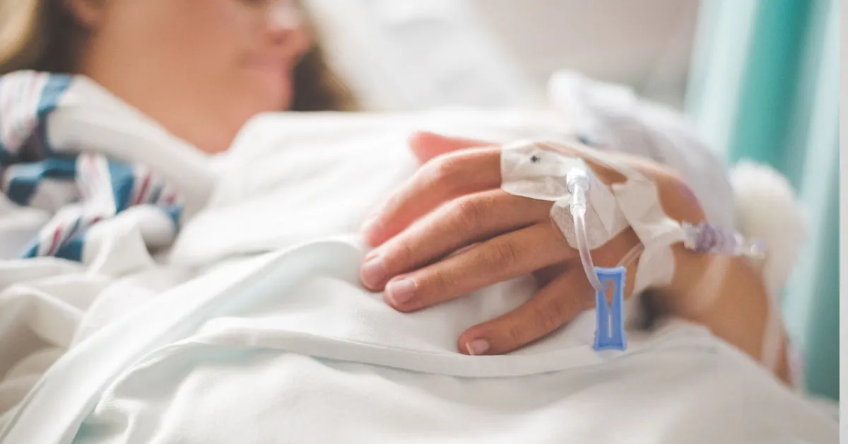Pessoa hospitalizada segurando a mão sobre o lençol, representando o auxílio-doença e a aposentadoria por invalidez