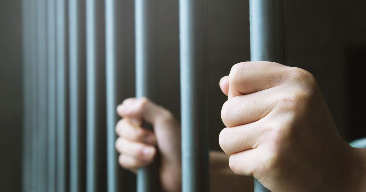 Pessoa segurando grades de prisão representando condenação criminal e seus efeitos no trabalho