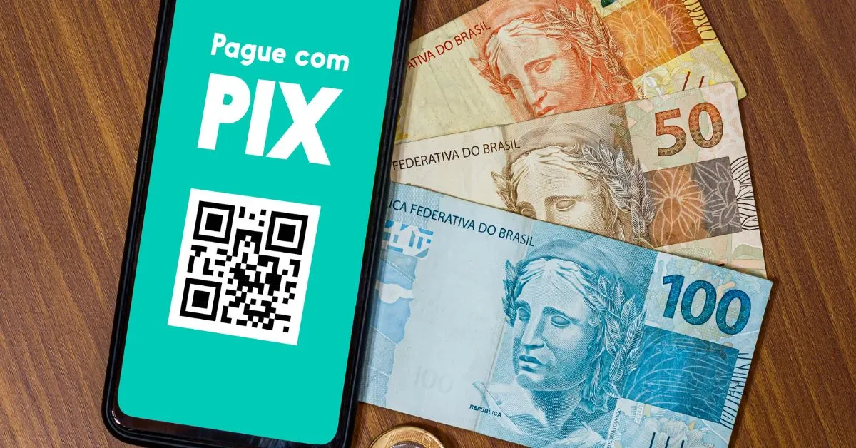 Tela de celular com a frase "Pague com Pix" e QR Code ao lado de notas de real, representando situação de cancelar um Pix por erro, golpe ou pagamento indevido