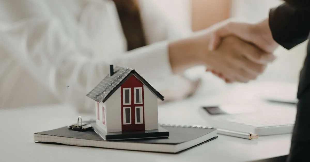 Imagem de maquete de imóvel e aperto de mãos, representando negociação de imóvel durante processo de inventário.